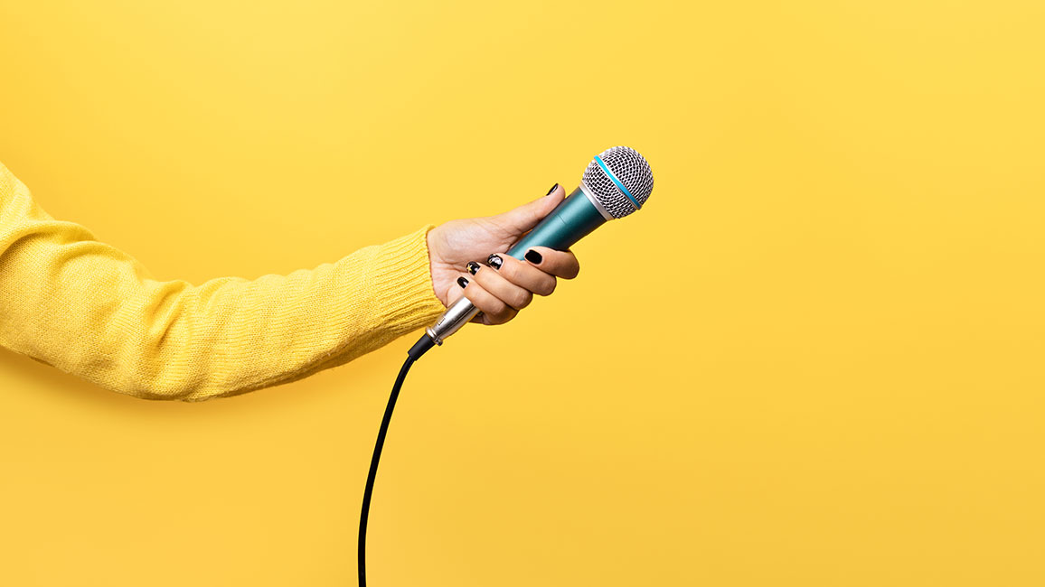 Eine Hand hält ein Mikrofon über einen gelben Hintergrund