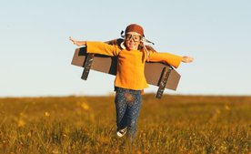 Kind läuft mit gebastelten Flügeln über ein Feld