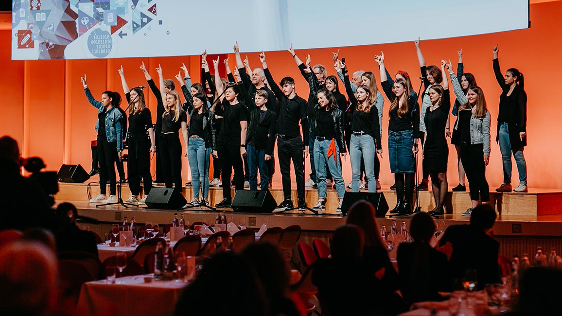 Schulchor "Claras Voices" steht mit erhobenen Händen und ausgestreckten Fingern auf der Bühne