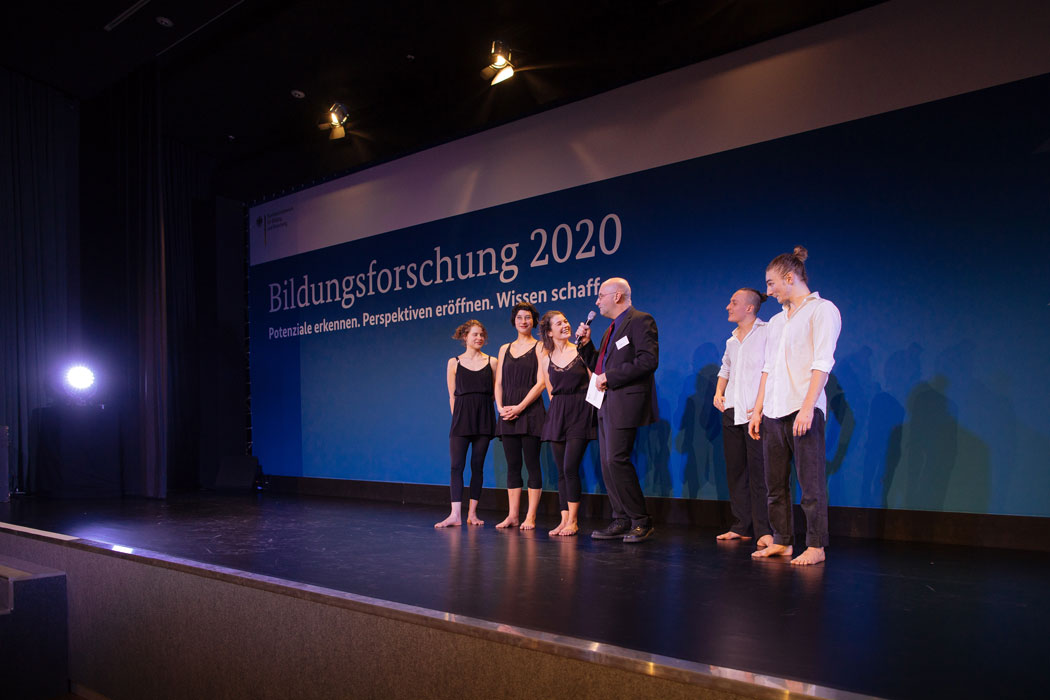 Fünf Jugendliche stehen auf der Bühne, in der Mitte steht der Moderator mit einem Mikrofon in der Hand