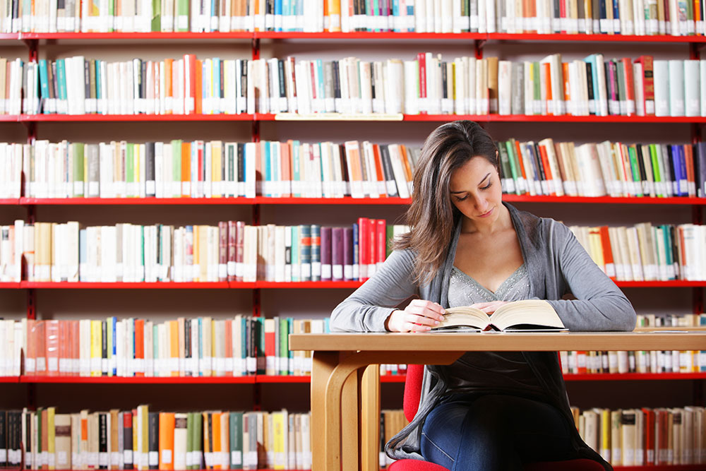 Studentin sitzt lesend vor einer Bücherwand